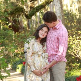 Mom-to-be in a flowing gown posing among lush greenery during a park maternity photoshoot by Katerina Krjanina.