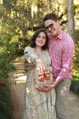 Pregnant woman glowing in a flowing dress, posing outdoors in a sunlit park for a professional maternity photoshoot by Katerina Krjanina.