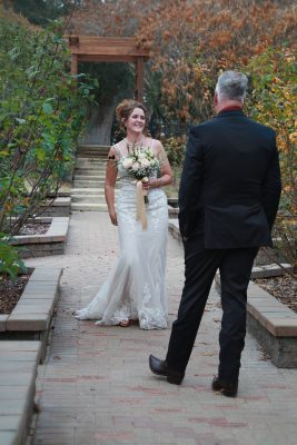 Bride and groom posing on a garden path at Washington Oaks Gardens State Park, surrounded by blooming flowers and tall trees.