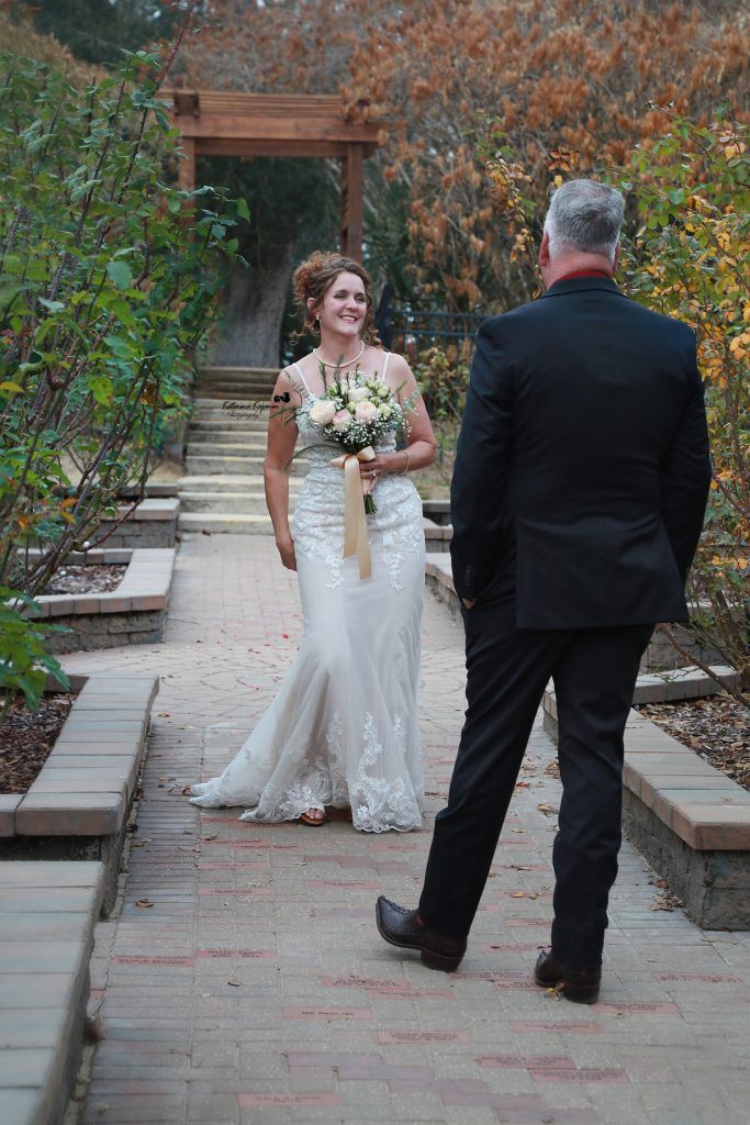 Bride and groom posing on a garden path at Washington Oaks Gardens State Park, surrounded by blooming flowers and tall trees.
