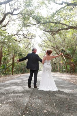 Bride and groom posing on a garden path at Washington Oaks Gardens State Park, surrounded by blooming flowers and tall trees.