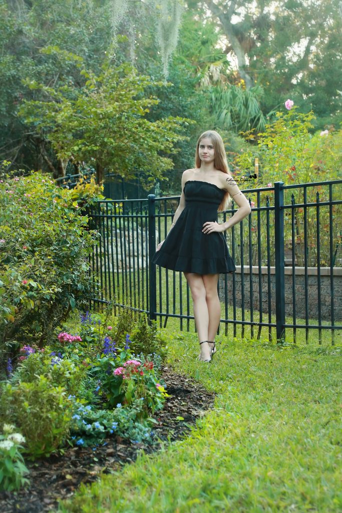 Graduate in cap and gown at Washington Oaks Gardens State Park with garden and coastal scenery.