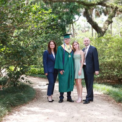 Graduate in cap and gown at Washington Oaks Gardens State Park with garden and coastal scenery.