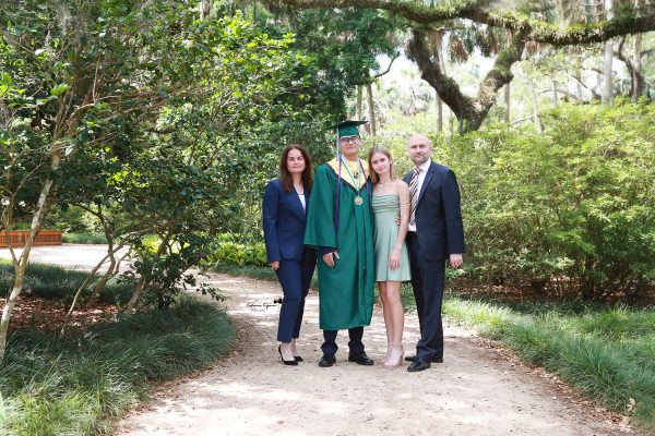 Graduate in cap and gown at Washington Oaks Gardens State Park with garden and coastal scenery.