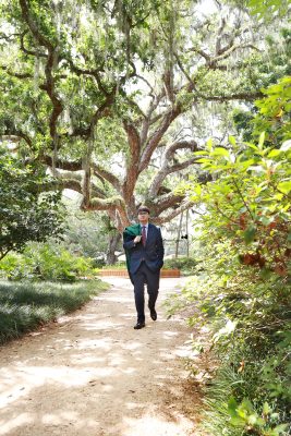 Graduate in cap and gown at Washington Oaks Gardens State Park with garden and coastal scenery.