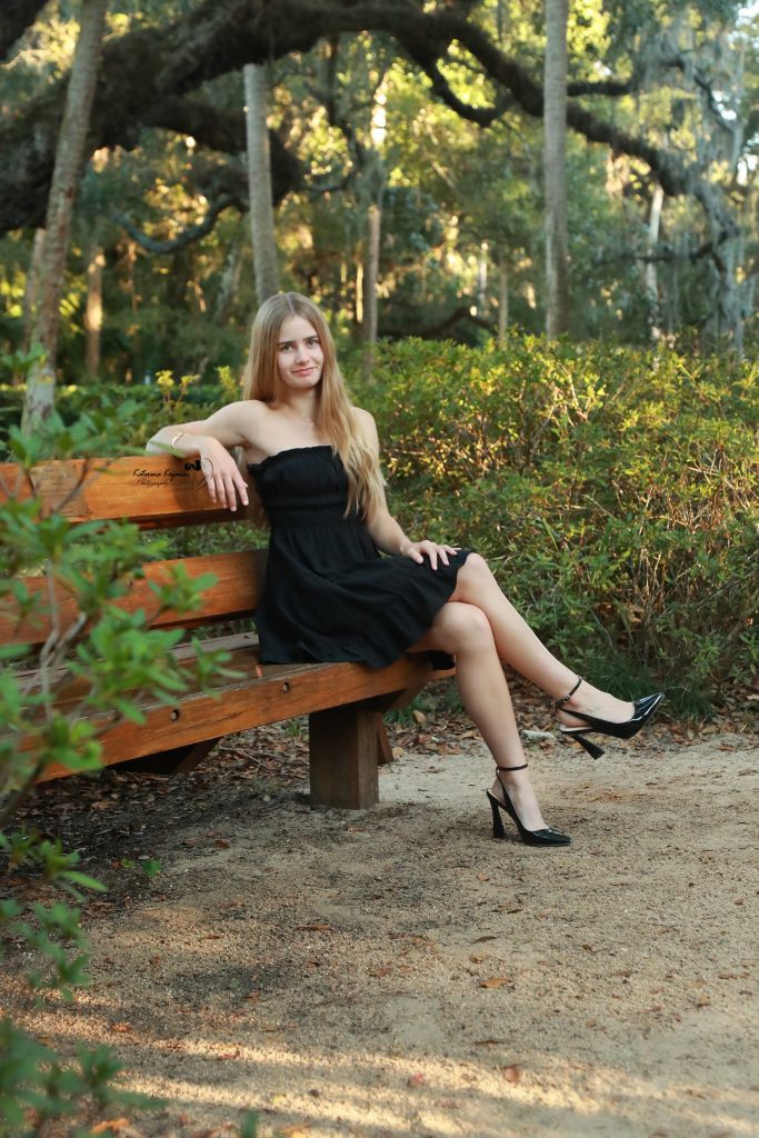 Graduate in cap and gown at Washington Oaks Gardens State Park with garden and coastal scenery.